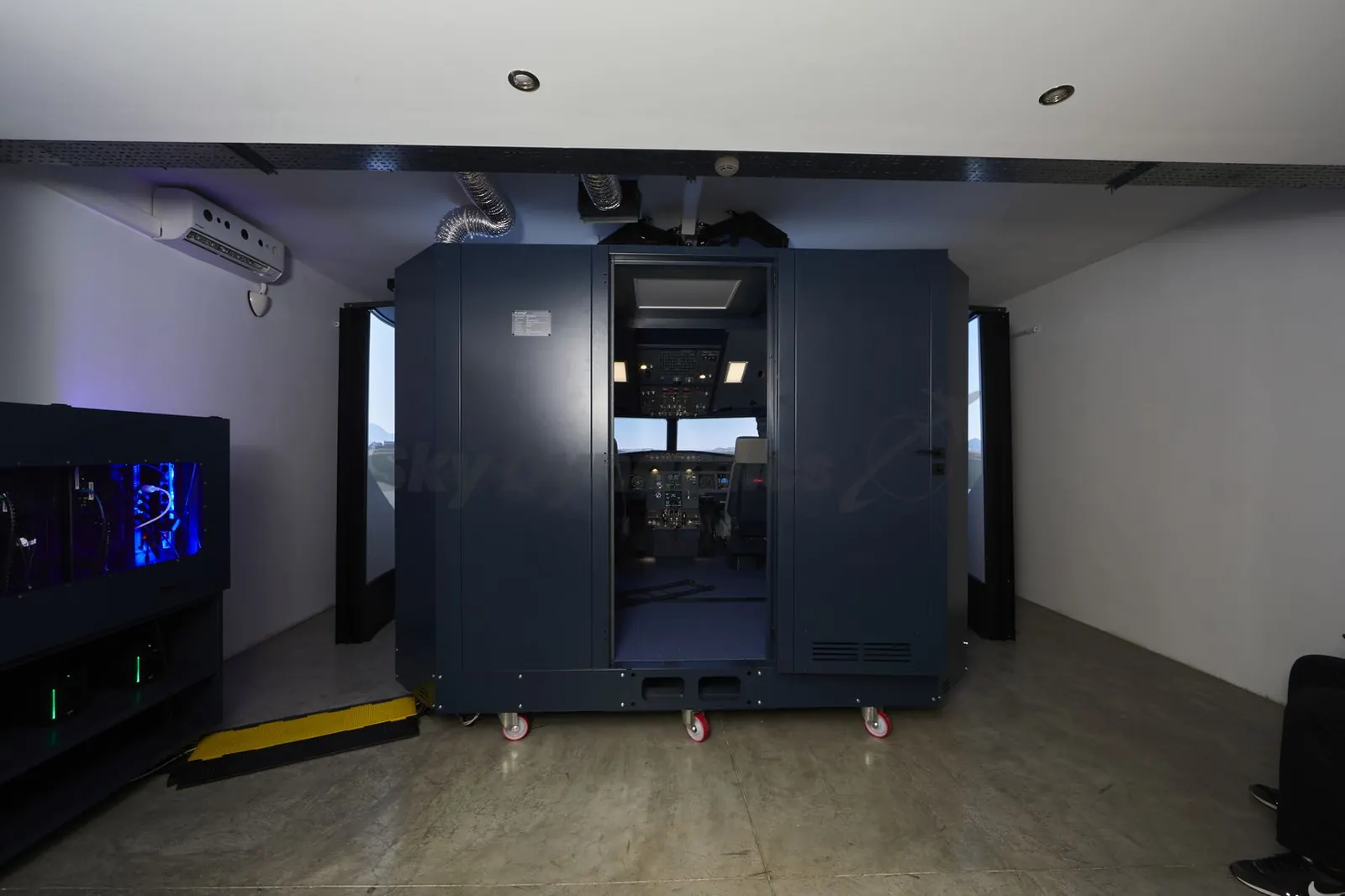 SkyDynamics Airbus A320 FNPT II seen from outside: the enclosure with its door open onto the flight deck, and the computer rack on the left