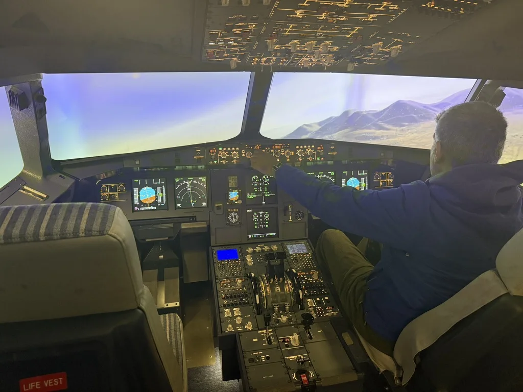 A pilot, seen from behind, reaches for the autopilot panel on the flight deck of the SkyDynamics A320 FNPT II simulator