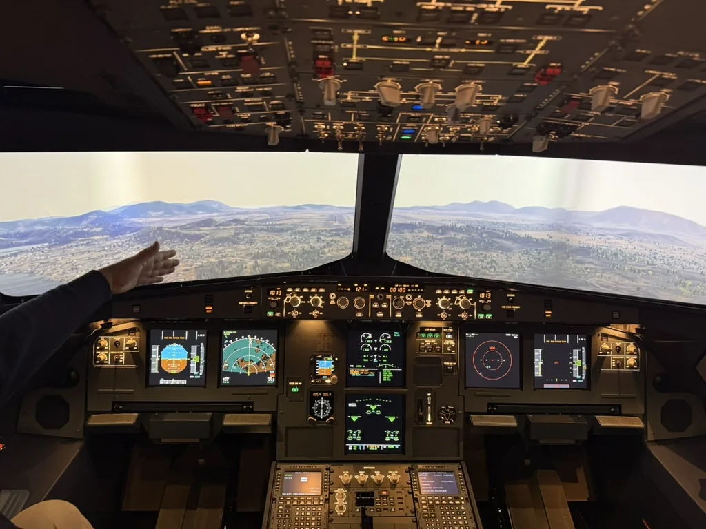 Flight deck of the A320 FNPT II simulator in flight over hilly terrain, all displays lit