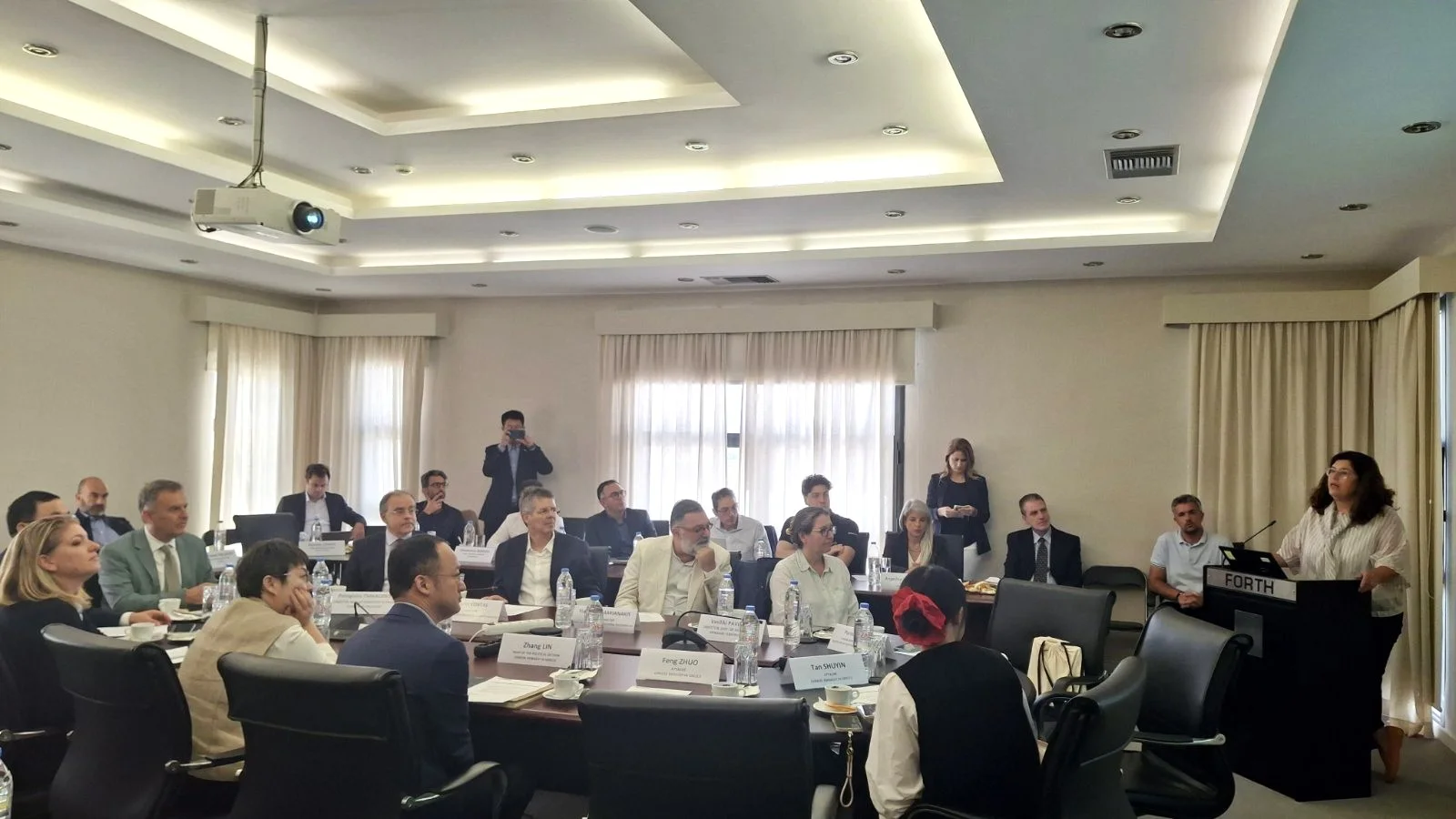 A presentation from the FORTH lectern to the participants of the visit, seated around the table
