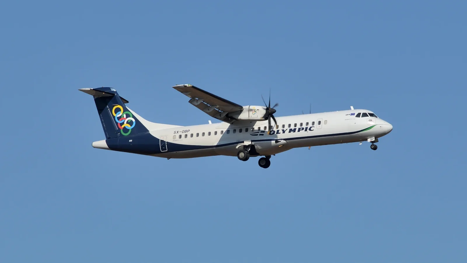 An Olympic Air ATR 72 in flight against a clear blue sky, landing gear down