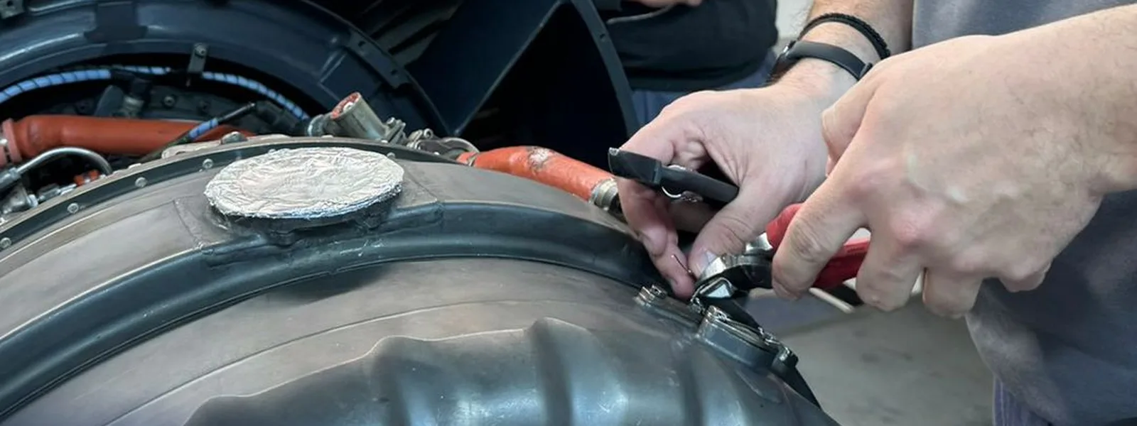 Hands safety-wiring a fastener on an aircraft engine during maintenance training assessment